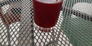 Red Zobo drink in a clear glass on a grey, metal mesh table.