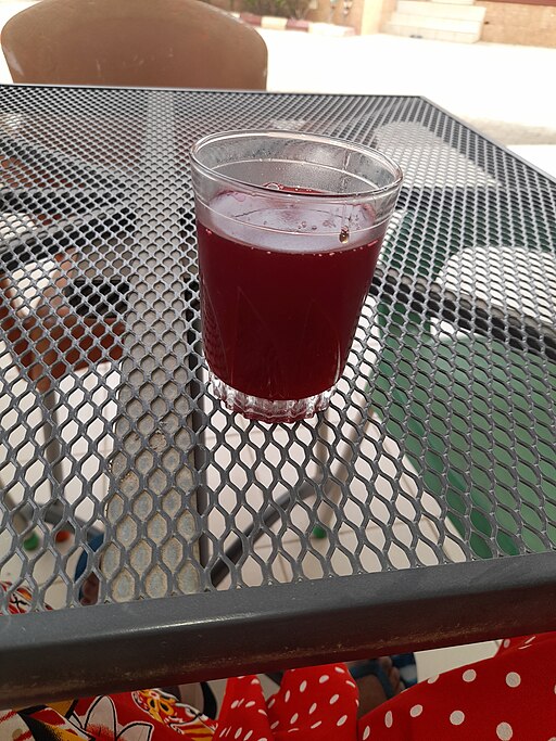 Red Zobo drink in a clear glass on a grey, metal mesh table.